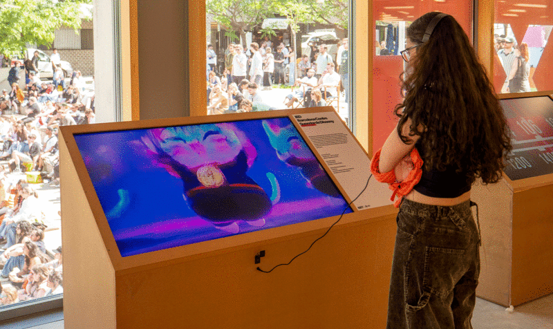 Una chica observando una pantalla insertada en un tótem que emite un cortometraje