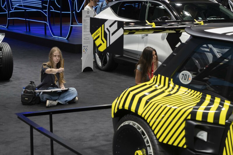 Una estudiante sentada en el suelo boceteando un coche amarillo y negro en primer plano