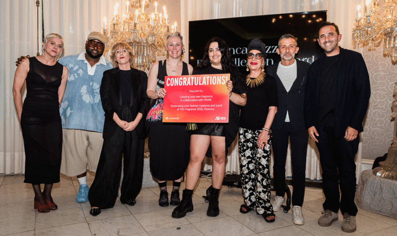 Entrega de premios con la ganadora en el centro y personalidades del jurado en los laterales delante de una pantalla