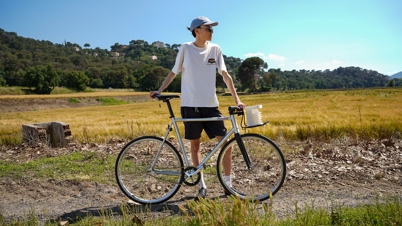 Un ciclista en el campo en un día soleado. La bicicleta lleva un dispositivo cilíndrico blanco colgado del manillar 