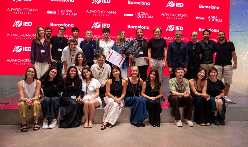 Una veintena de personas subida sobre un escenario posando para una foto de grupo con una pantalla roja de fondo con el logo IED Barcelona