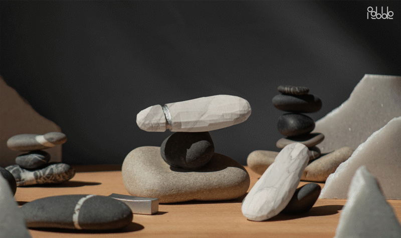 Plano detalle de una mesa con piedras dispuestas y una pequeña torre en el centro coronada por un dispositivo AIG de color piedra y forma inspirada en una punta de sílex