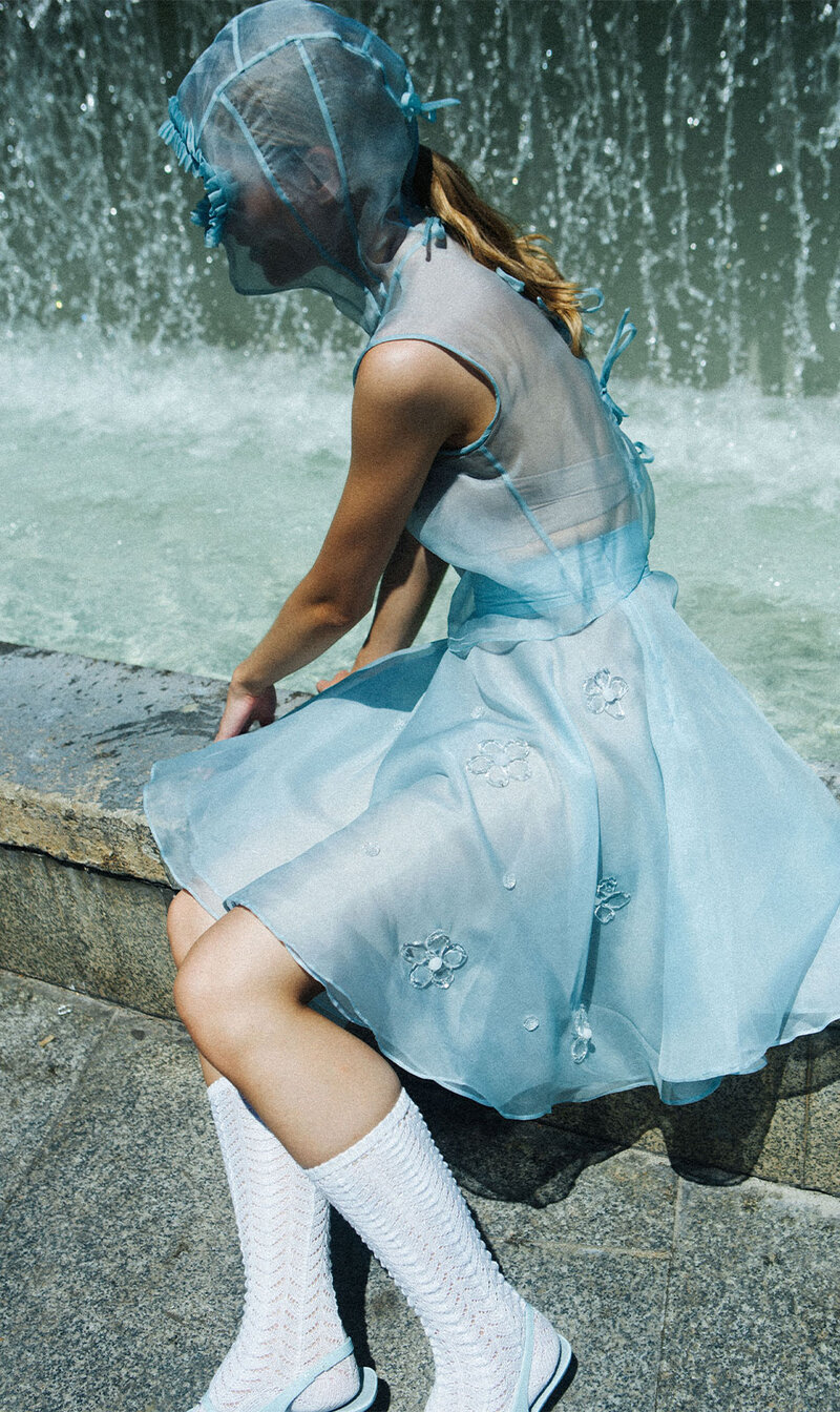 Modelo femenina sentada delante de una cortina de agua con un vestido azul celeste con transparencias