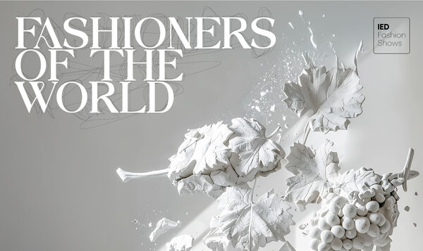 Un racimo de uvas de yeso blanco sobre un fondo gris junto a las letras del desfile FASHIONERS OF THE WORLD
