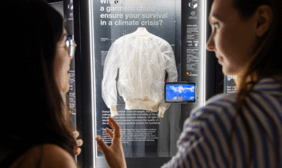 Dos mujeres admirando una chaqueta blanca exhibida en una vitrina en el centro de la imagen