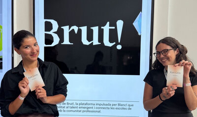 Dos chicas sosteniendo un programa de papel delante del cartel de un festival de diseño
