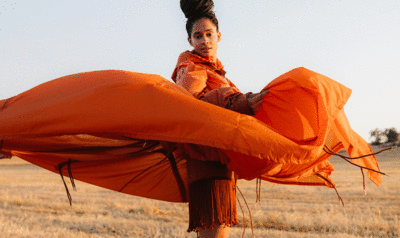 Una chica alza al vuelo su vestimenta de color naranja en un campo de trigo